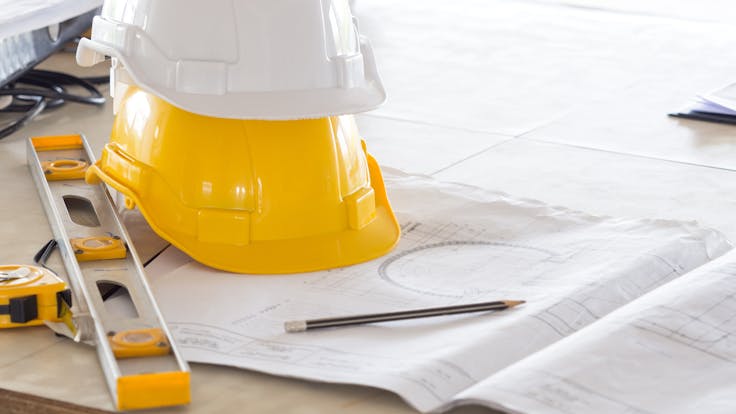 Safety helmet for engineer and architect on working desk/table with drawing/blueprint and tools at job site, engineer/architect for construction work concept - building codes and standards for construction.