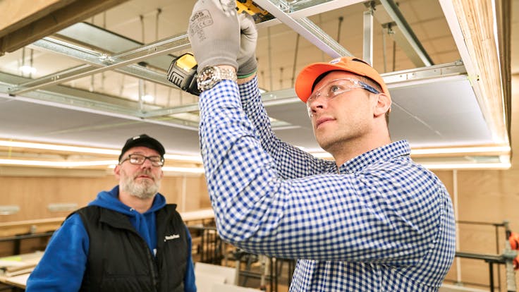 Trainee installing grid in Rockfon Training Centre Daventry Training Course brochure, trainee installing grid with a screwdriver in the systems training area