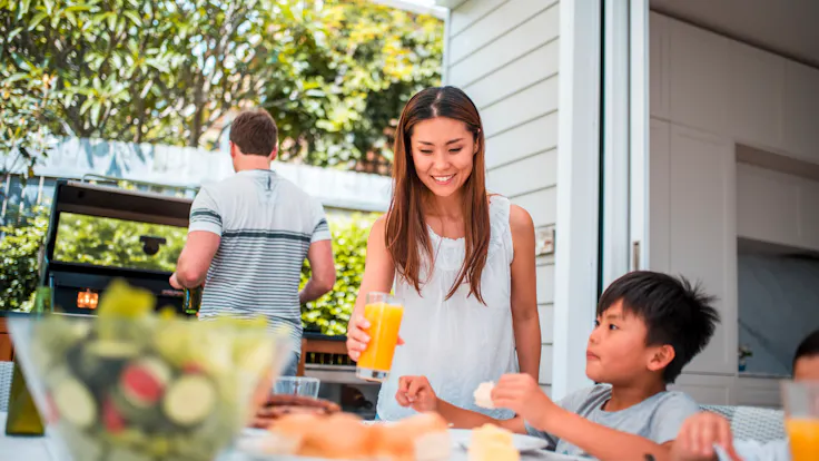 Family with two children having lunch outdoors. They are enjoying time together. Father is using barbecue grill.