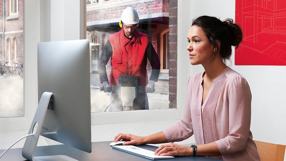 Woman working in office with a construction worker outside her window making noise
