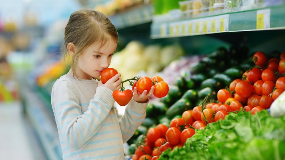Little girl in supermarket smelling fresh tomotoes