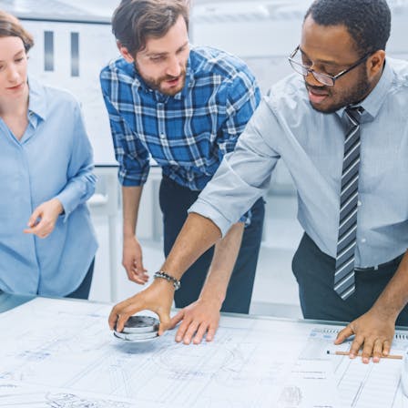 People in office standing around a table, discussing, planning. Stock image.