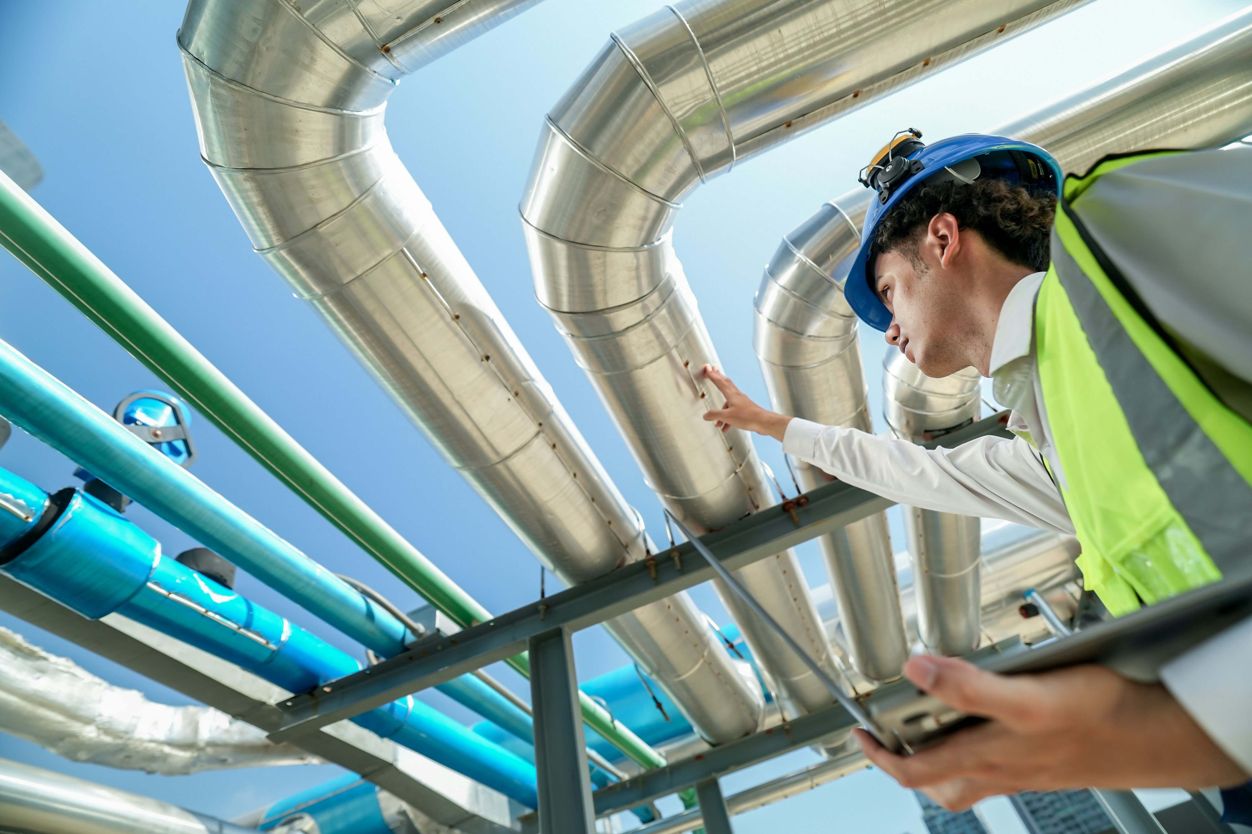 Industrial engineer adjusting pipeline valve with radio communication on construction site. Engineer on urban construction site using radio to coordinate with team on a sunny industrial rooftop.