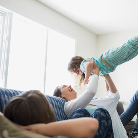 People indoor living room
Playful mother lifting daughter overhead on sofa