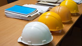 Four hard hats on a wooden desk next to documents - building codes and standards for construction.