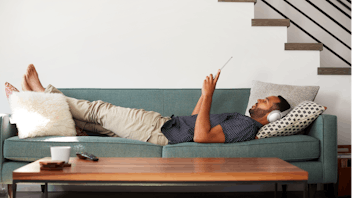Man Lying On Sofa At Home Wearing Headphones; Shutterstock ID 1125901364;  Used for Sustainability Report 2018.
20s; at home; entertainment; headphones; horizontal; indoors; lounge; lying; male; man; online; people; person; relaxed; relaxing; sofa; tablet
