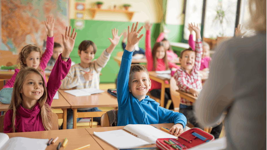 Children sitting in classroom with raised hands