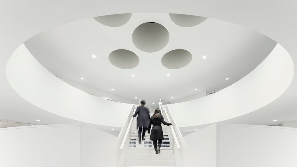 A statement staircase in a public building with white seamless acoustic ceilings and walls