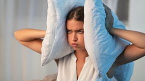 Annoyed Young Lady Covering Ears With Pillow Irritated Because Of Noise At Home.