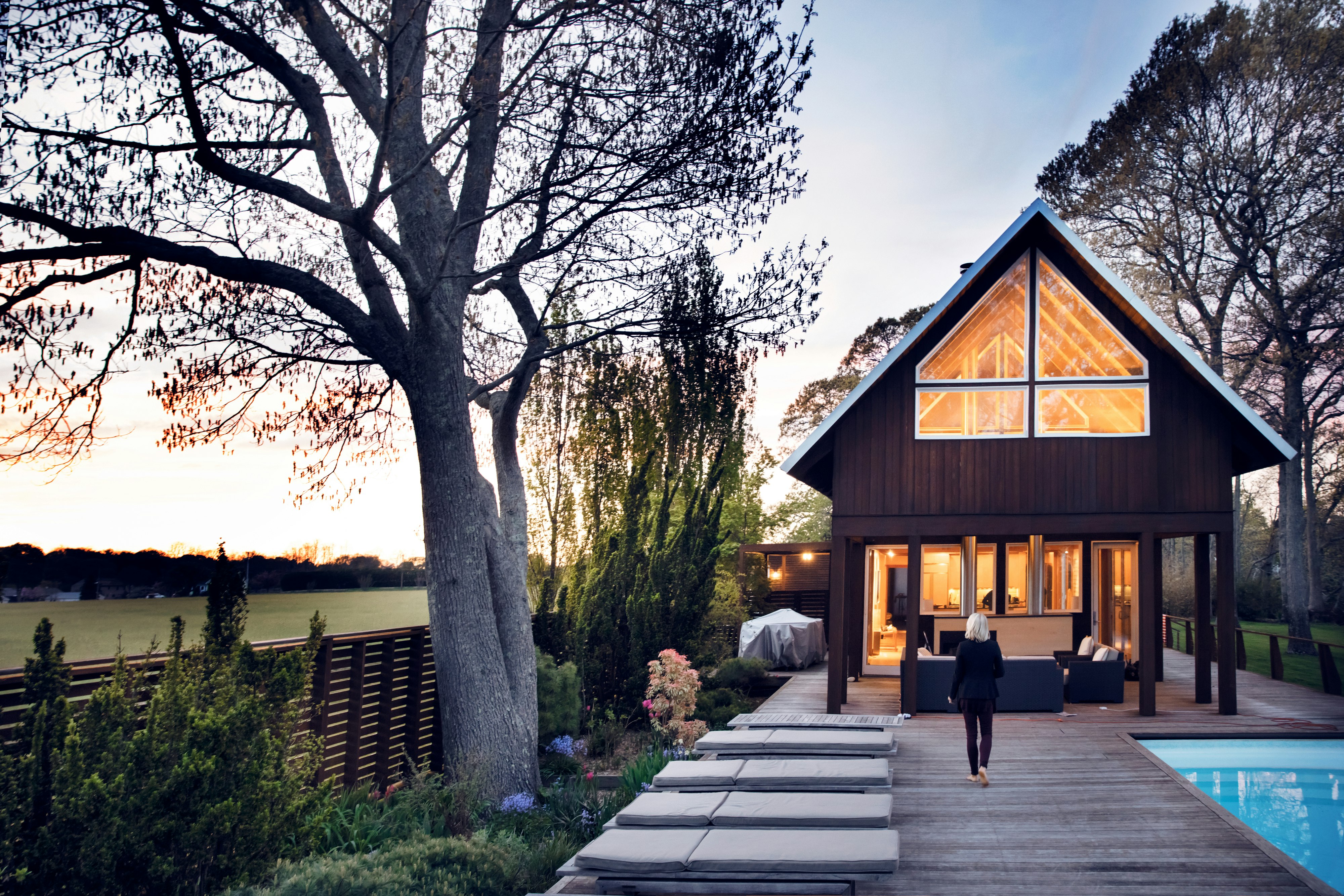 House outdoor Rear view of woman walking by swimming pool. wood house. Outside.