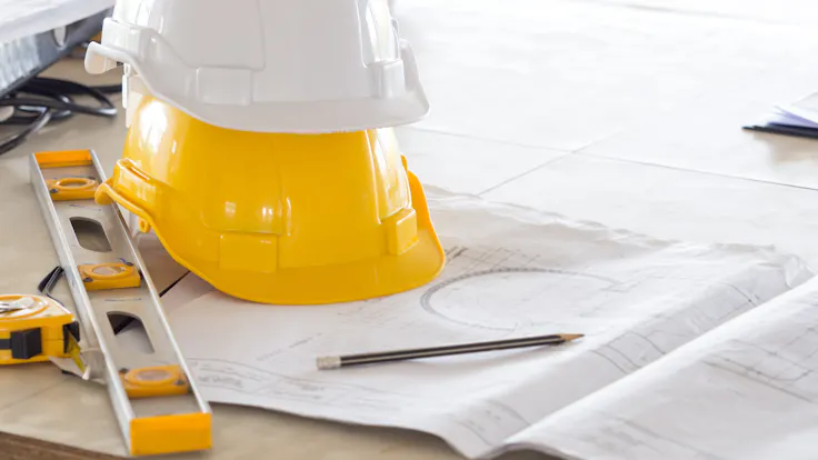Safety helmet for engineer and architect on working desk/table with drawing/blueprint and tools at job site, engineer/architect for construction work concept - building codes and standards for construction.