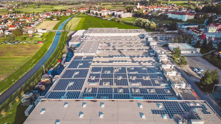 Aerial view of a large factory in the suburbs with solar panels covering the roof top