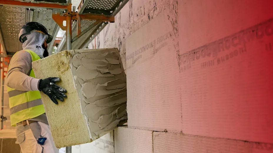 Ein Handwerker bringt ROCKWOOL Dämmung bei einer Sanierung auf einer bestehenden Wand an.