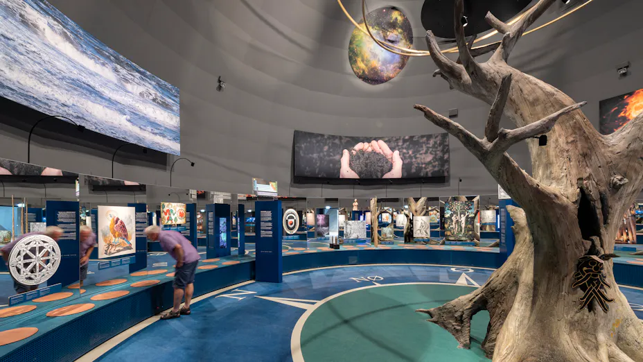 Naturkraft exhibition space featuring a dome-shaped Rockfon Color-all acoustic ceiling installation, with a central tree sculpture, suspended planet models, and interactive displays arranged around the circular gallery.