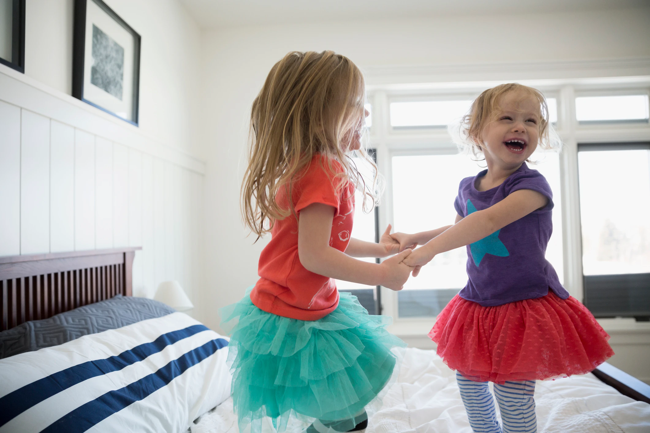 Playful sisters holding hands and jumping on bed. People, children, indoor, acoustics