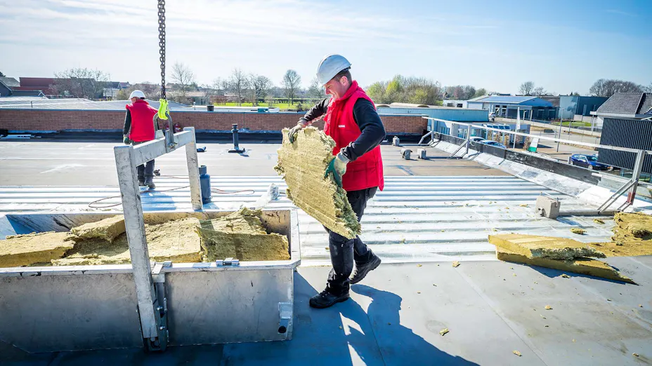 Vakmensen voeren gebruikte steenwol af van een plat dak van een bouwproject.