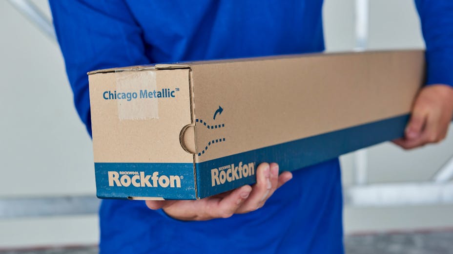 Person holding a box of Chicago Metallic suspension grid profiles from Rockfon